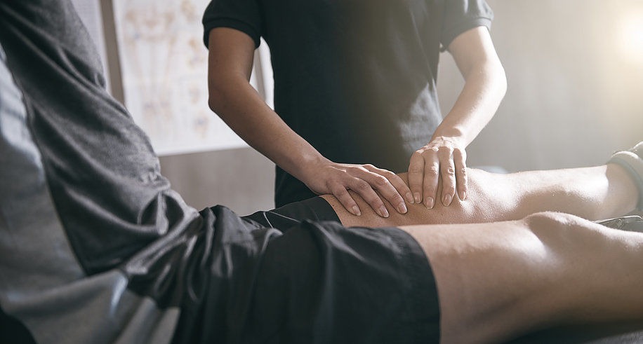 Sportmassage - masseur behandelt de beenspieren van een sporter